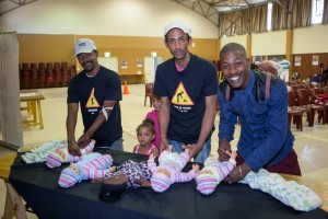 Three fathers learn nappy (diaper) changing using dolls at Mosaic's "Father and Child Day."