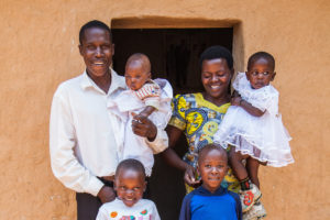 A man, a woman, and 4 children stand in front of a door, smiling.
