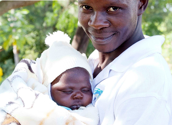 A father smiles and holds his infant in Mozambique