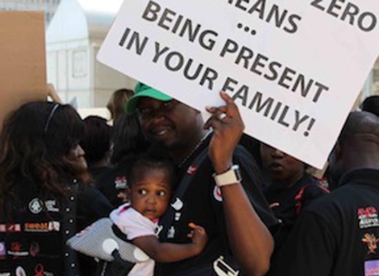 A man in South Africa holds his baby daughter and a banner about involved fatherhood at the march for the International Conference on AIDS and Sexually Transmitted Infections in Africa