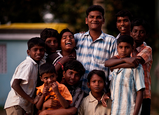 A group of boys and young men crowd together and smile at the camera in India