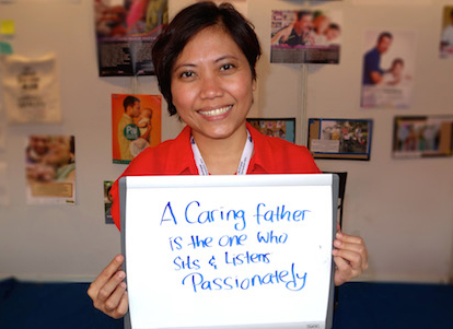 A participant at the MenEngage Global Symposium in Delhi holds a sign she wrote that reads "A caring father is one who sits and listens patiently"