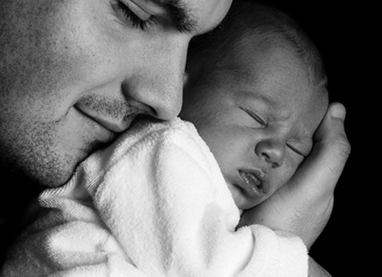 A black-and-white image of a father holding his newborn baby close