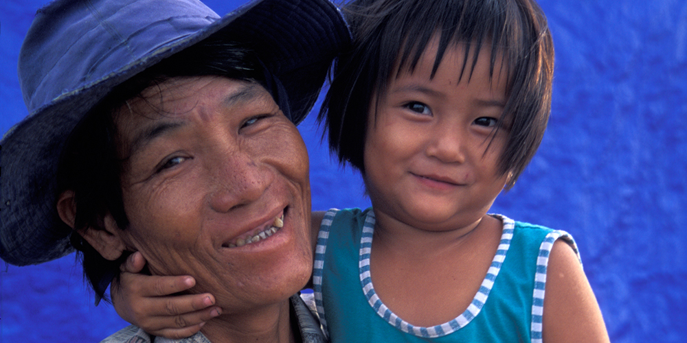 A Vietnamese man smiles while holding his young daughter in his arms.