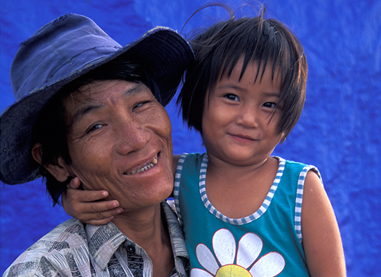 A Vietnamese man smiles while holding his young daughter in his arms.