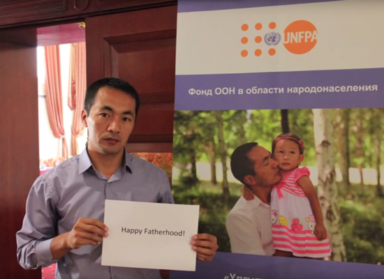 A man holds a sign that reads "Happy Fatherhood."