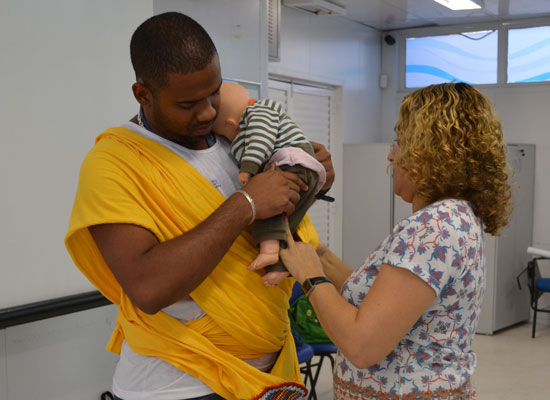 A father learns how to carry a baby in a sling, using a doll, in a MenCare+ workshop in Brazil.