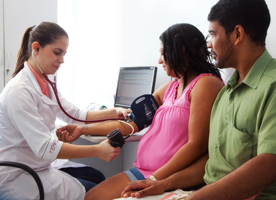 A health worker takes the blood pressure of a pregnant women who is accompanied by her partner.