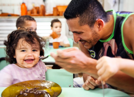 A smiling father feeds his laughing daughter.